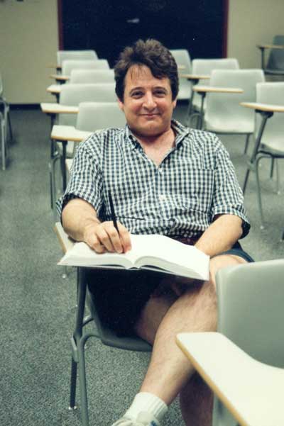 John Dobelman sitting in student's desk in classroom.